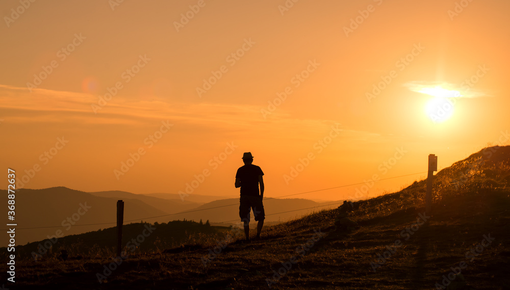Portrait  of man silhouette standing at the top of the mountain looking the landscape on sunset background