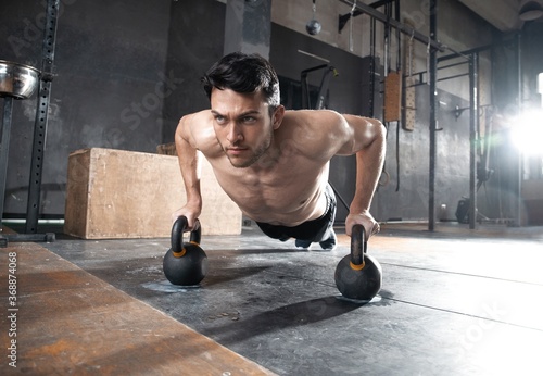 Handsome muscular man doing pushup exercise with dumbbell in a crossfit workout