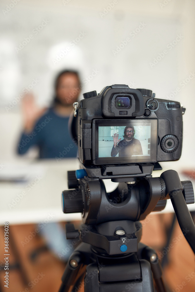 New online course. Young happy male teacher looking at camera and waving while giving online lesson through webcam at home. Recording video blog