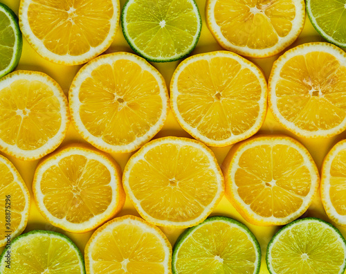 Sliced lemons and limes in round slices on yellow background.