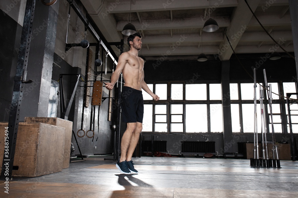 Fototapeta premium Young sportsman doing jump rope workout in gym
