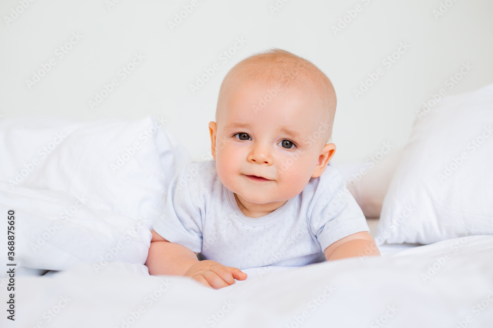 Cute baby boy smiling lies in the bed of the house. bedding for children Cute baby boy smiling lies in the bed of the house. bedding for children
