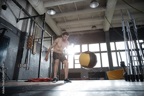 Fit man throwing medicine ball doing ball slam against gym floor or shoulder press upper body workout exercise. Cross training at fitness center.