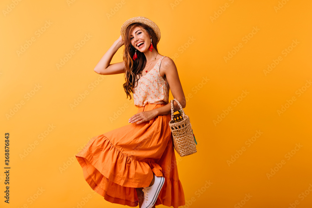 Joyful european lady in summer hat dancing on yellow background
