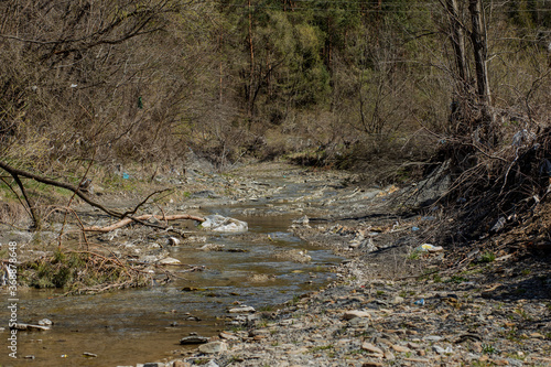A beautiful small stream is littered with a bunch of garbage, empty bottles, cellophane bags, plastic cans