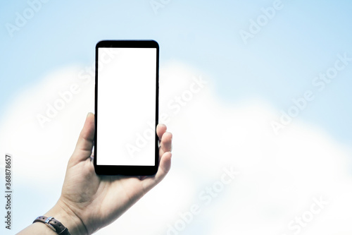 Girl holding a phone with a white screen against the sky. Mockup.
