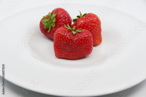 Three red ripe strawberries on a white plate. Strawberries isolated on a white background.