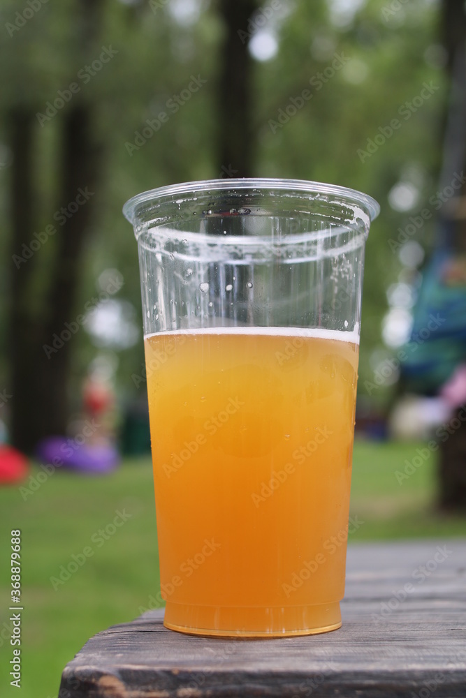 A plastic glass with beer stands on a wooden table in nature
A plastic glass with beer stands on a wooden table in nature