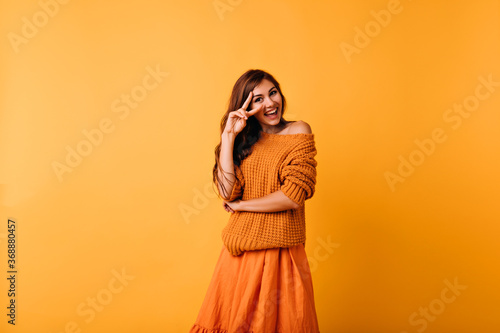 Stunning caucasian girl in trendy orange sweater smiling to camera. Indoor photo of wonderful young woman wears bright clothes.