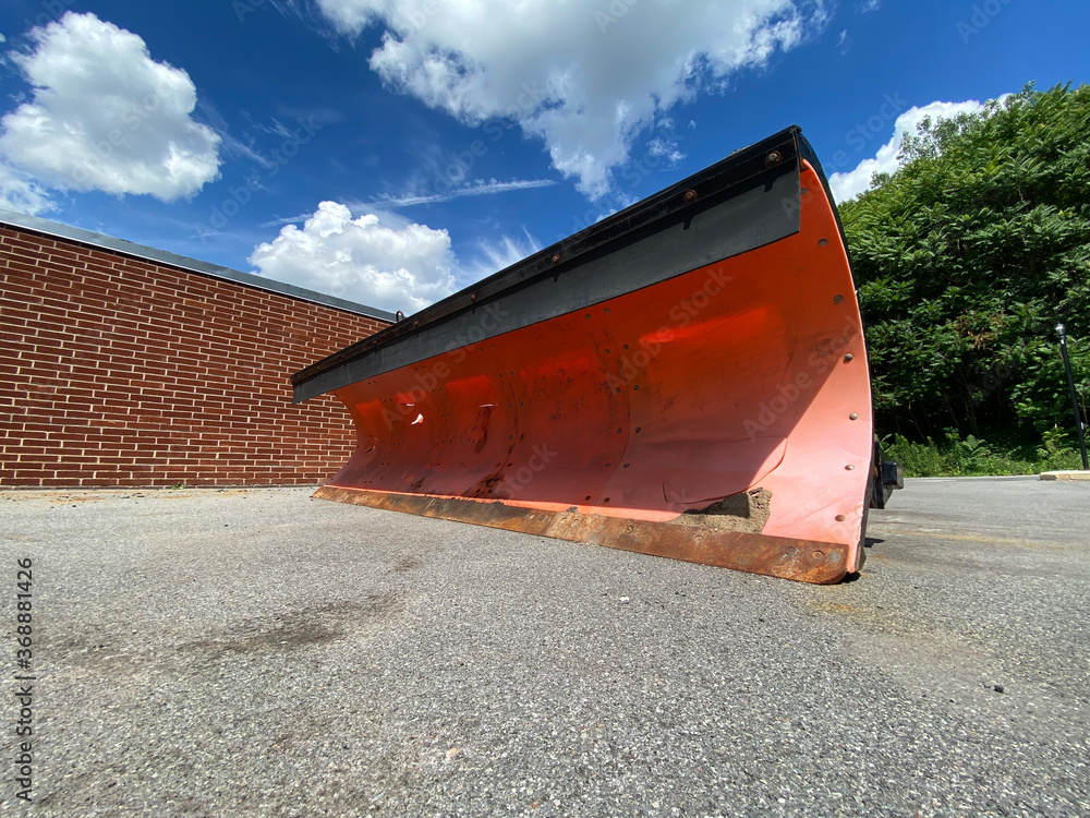 Snowplowing truck head next to brick wall and forest Snowplowing truck head next to brick wall and forest