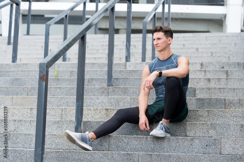 Portrait of a confident sporty man. Young sportsman sitting outdoors after good jogging workout. Young man in sportswear. relax after training. guy sits on the stairs. Pensive strong guy sitting