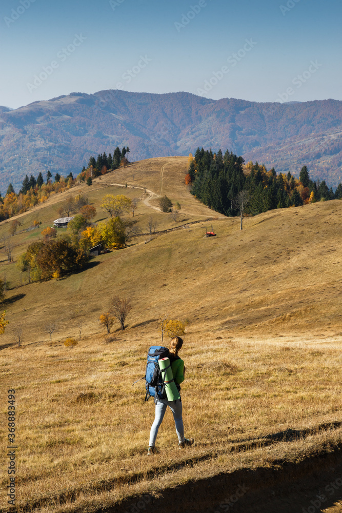 Female hiker with big backpack walking in mountains in autumn