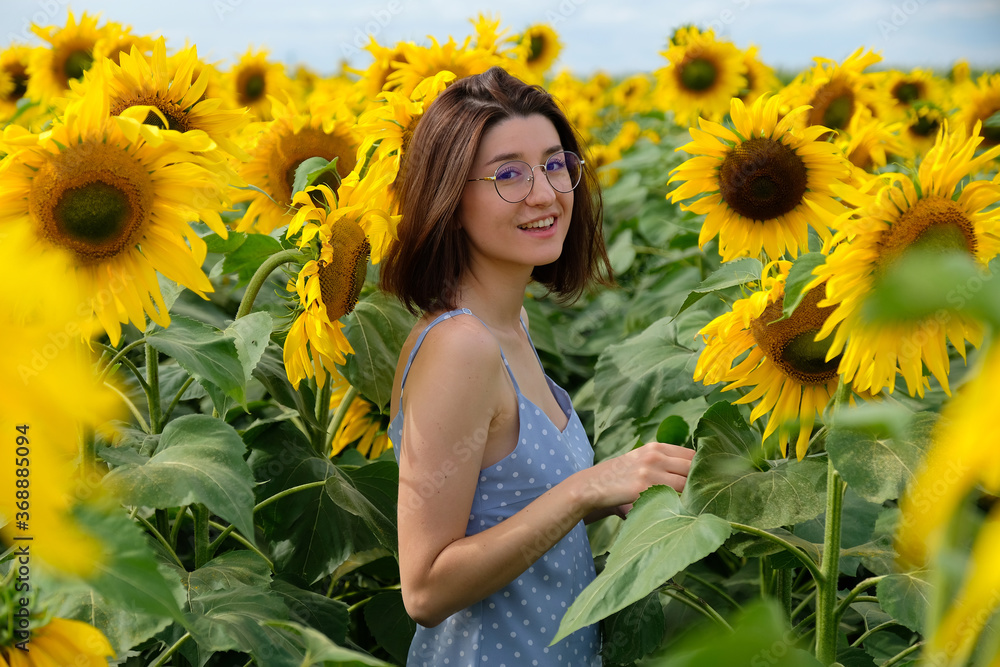 Young joyful girl in blue dress walking in sunflowers field at sunset. Young joyful girl in blue dress walking in sunflowers field at sunset.