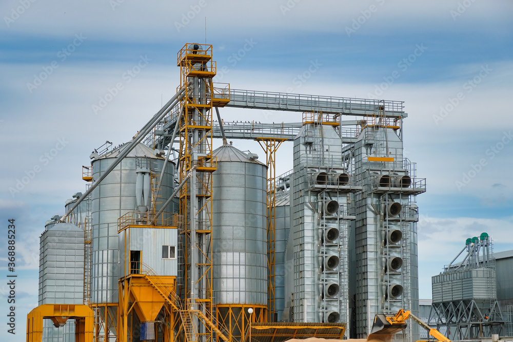 Agribusiness concept. Metal silos for grain storage, drying, cleaning agricultural products, flour, cereals and grain on agro-processing and manufacturing plant. Agribusiness concept. Metal silos for grain storage, drying, cleaning agricultural products, flour, cereals and grain on agro-processing and manufacturing plant.