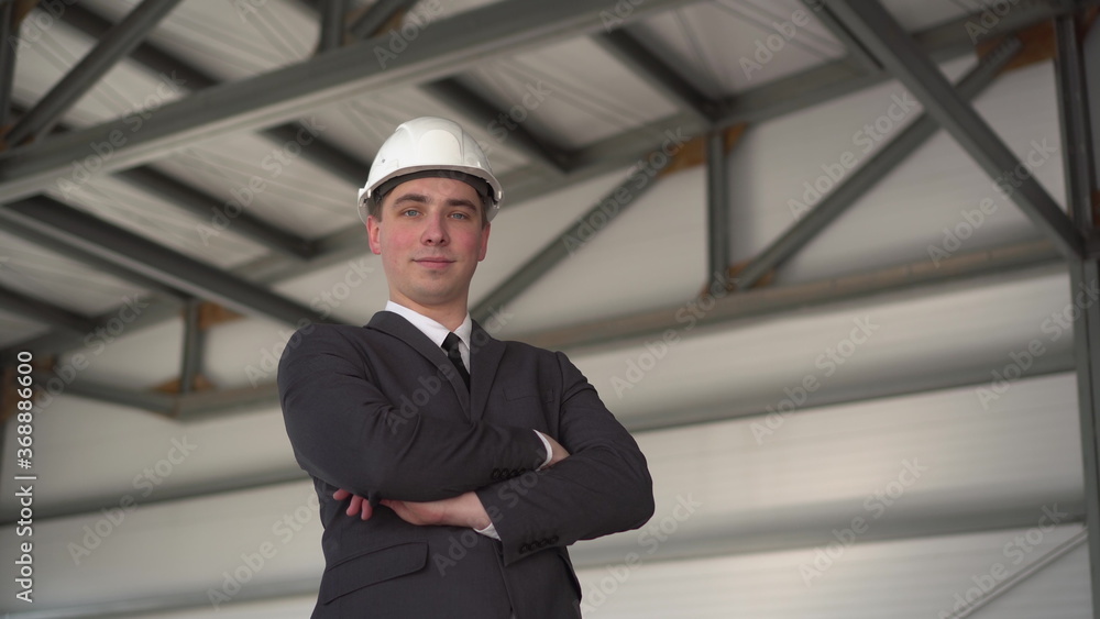 A young man in a protective helmet and shows a thumb at a construction site. The boss in a suit looks at the camera.