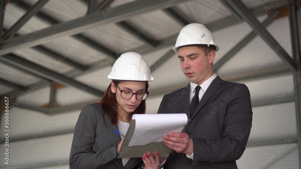 Young man and woman in helmets with documents at a construction site. Businessmen in suits conclude an agreement. A woman signed documents. Young man and woman in helmets with documents at a construction site. Businessmen in suits conclude an agreement. A woman signed documents.