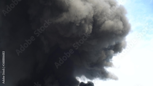 Black smoke rises into the sky. A big chemical fire at a factory building. Thick black smoke covers the sky.