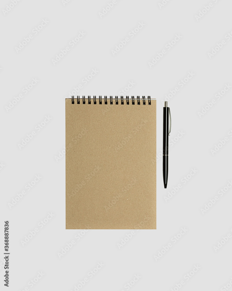 Blank spiral notepad mockup template with kraft paper cover with black glossy pen isolated on light gray background. Blank spiral notepad mockup template with kraft paper cover with black glossy pen isolated on light gray background.