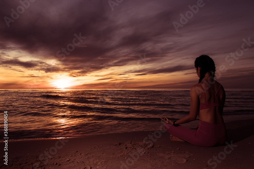 Silhouette of young woman wearing exercise clothes practicing yoga on the beach at sunset or sunrise. women do yoga. women exercising yoga in the beach.Young girl meditating in lotus posture.