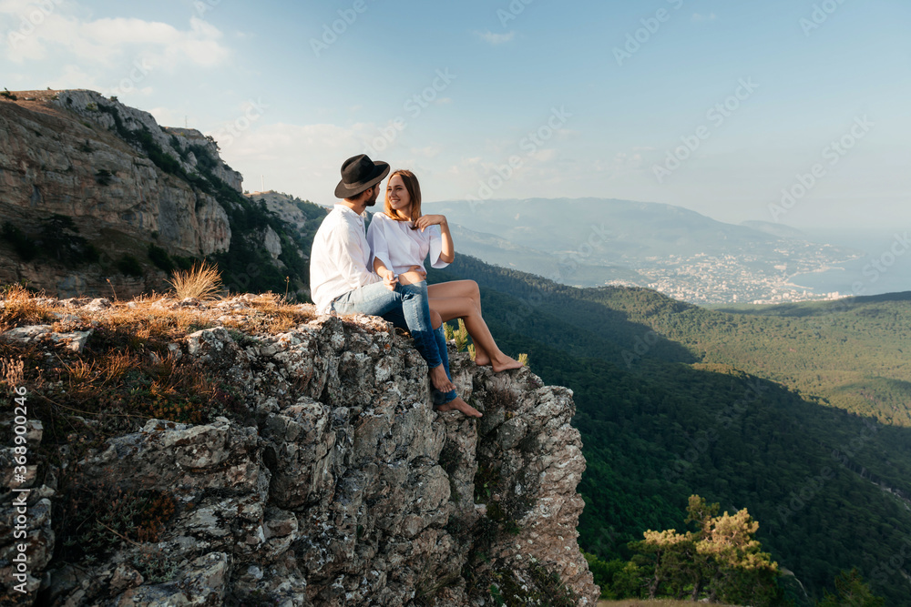 Attractive young loving couple of man in white shirt and blue jeans with girl in dress on sunny outdoor background in the green mountain landscape