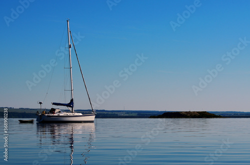 A prussian yacht anchored near the shore next to a small boat with paddles in full calm at dawn