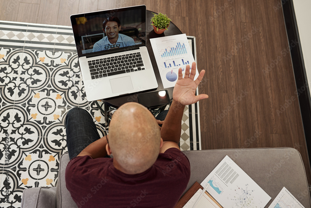 Naklejka premium Young bald entrepreneur actively gesturing when having online meeting with colleague,view from above