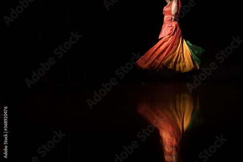 Transgender Asian person doing traditional Indian dance in front of a dark black background. Dressed up like an Indian Goddess. photo
