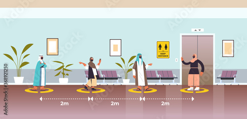 arab businesspeople in protective masks keeping distance to prevent coronavirus pandemic social distancing concept people standing on yellow floor signs full length horizontal vector illustration