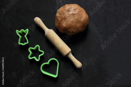 A dough ball, a rolling pin for dough and a cookie shape on a black background. View from above. Cooking ginger biscuits. Christmas atmosphere. Flatlay. Copy space for text. Pastries. Holiday