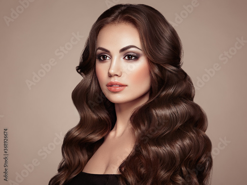 Brunette woman with long and volume shiny wavy hair . Beautiful model with curly hairstyle. Perfect make-up. Beauty style model
