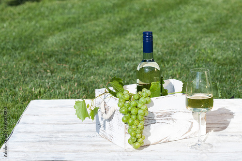 White wine on wooden white vintage table with green lawn on background photo