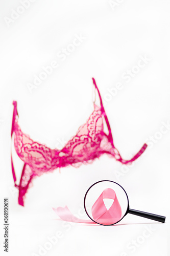 World cancer day. A pink bra on a white background, and a pink ribbon under a magnifying glass. Vertical orientation. Copy space photo