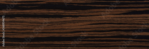 Unique ebony veneer background in dark color. Natural wood texture, pattern of a long veneer sheet, plank.
