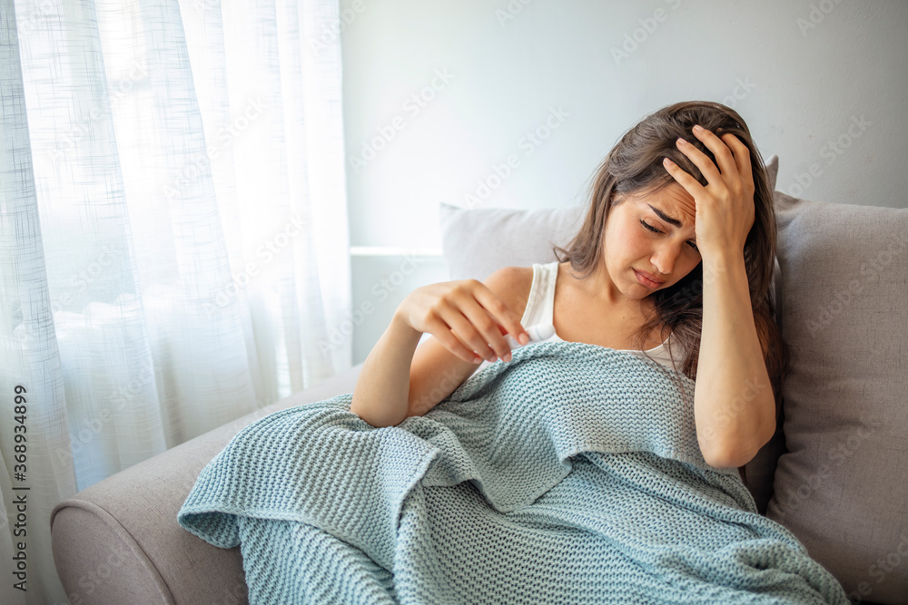 Young woman feeling worried while using thermometer and measuring her body temperature at home. Sickness, seasonal virus problem concept. Sick woman lying in bed with high fever. Young woman feeling worried while using thermometer and measuring her body temperature at home. Sickness, seasonal virus problem concept. Sick woman lying in bed with high fever.