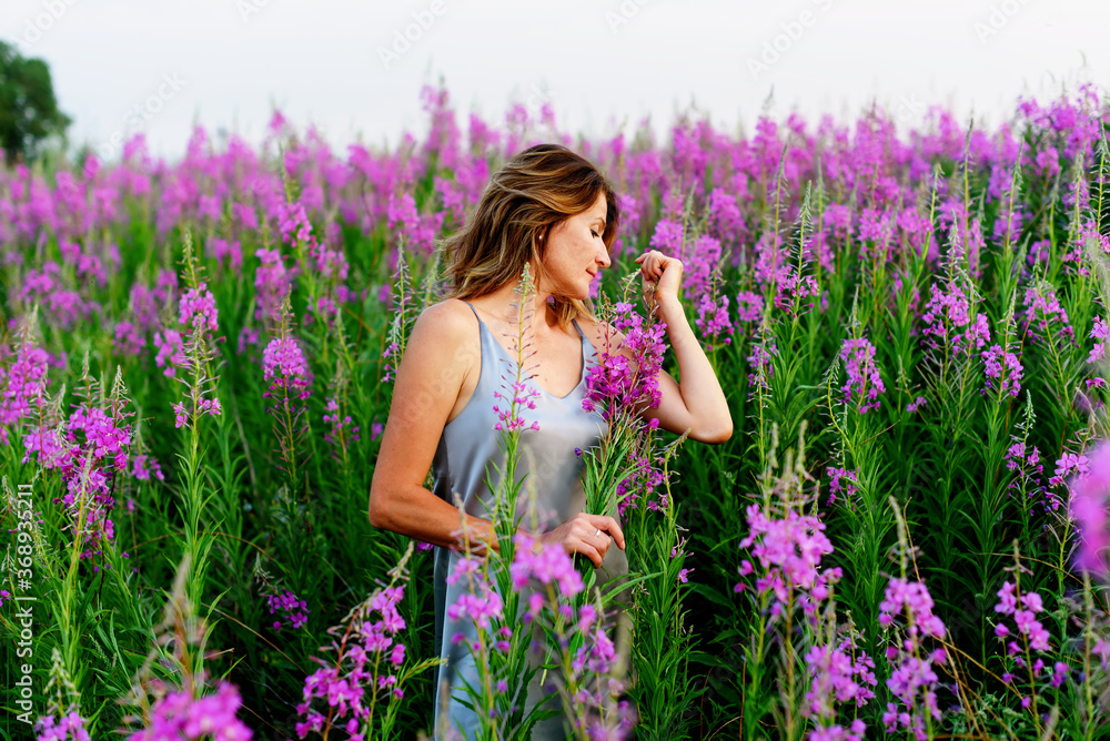 Beautiful woman in gray dress relaxes with bunch of flowers on fireweed meadow Beautiful woman in gray dress relaxes with bunch of flowers on fireweed meadow