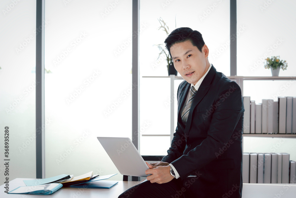Portrait of Asian smiling businessman in suit using laptop computer at desk in the office, man in workplace, doing business Portrait of Asian smiling businessman in suit using laptop computer at desk in the office, man in workplace, doing business
