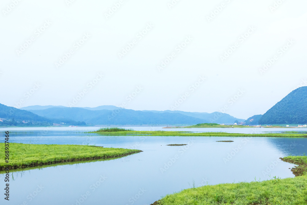 Peaceful and beautiful lake and green field background blue sky,early summer morning landscape.