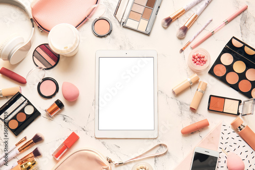 Composition with tablet computer and cosmetics on light background
