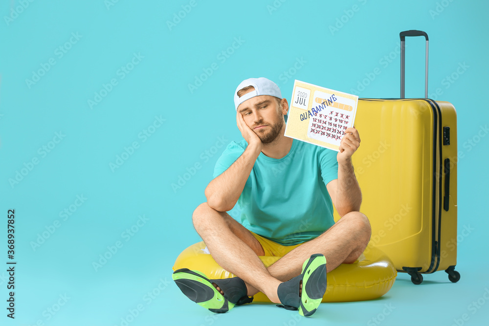 Sad man holding calendar with written word QUARANTINE and suitcase against color background. Vacation concept Sad man holding calendar with written word QUARANTINE and suitcase against color background. Vacation concept