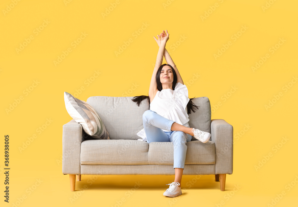 Young woman relaxing on sofa against color background