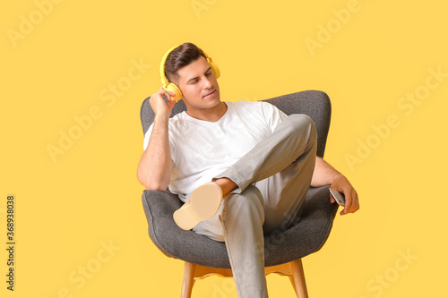 Young man listening to music while relaxing in armchair against color background