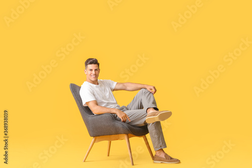 Young man relaxing in armchair against color background © Pixel-Shot