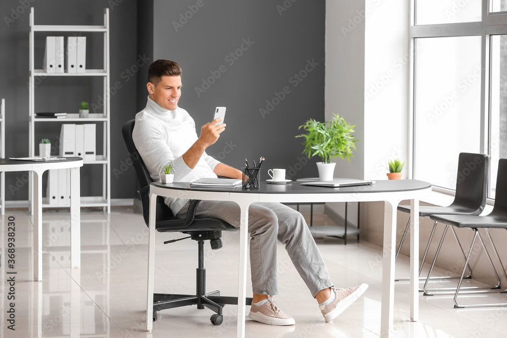Young man with mobile phone relaxing at workplace in office Young man with mobile phone relaxing at workplace in office