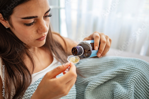Exhausted young woman preparing to drink spoonful of cough syrup while suffering from flu at home. Young Girl Drinking Medicine Syrup. Young woman taking medicine on spoon at home.