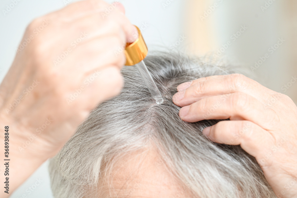 Obraz premium Senior woman using serum for hair loss treatment, closeup