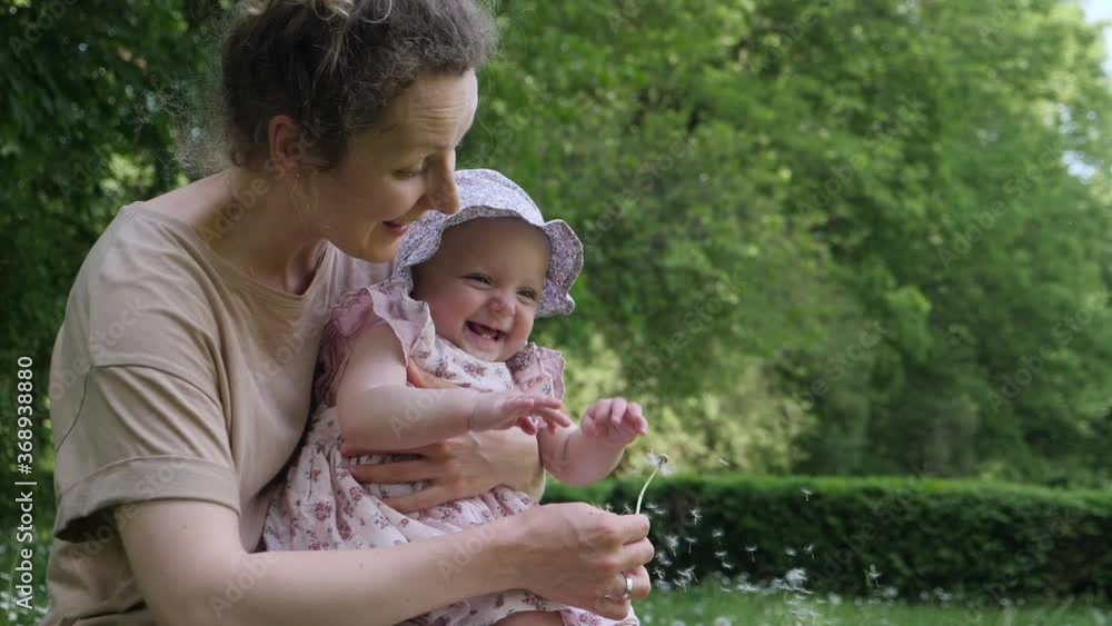Mother holds child on hands and plays with dandelion. Kid laughs in hands of mom in the park Mother holds child on hands and plays with dandelion. Kid laughs in hands of mom in the park