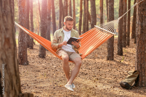 Young man with book relaxing in hammock outdoors
