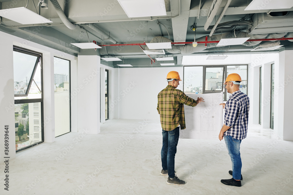 Two young construction engineers discusing blueprint of building and planning works for today Two young construction engineers discusing blueprint of building and planning works for today