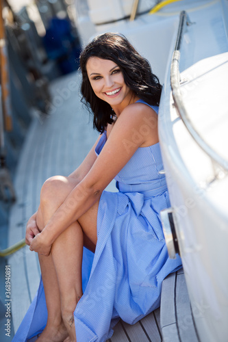 Beautiful woman resting on the boat. Laughing girl with tanned skin in seaport in sunny morning. Charming dark-haired lady smiling and enjoying summer vacation on favorite resort. © darkfreya