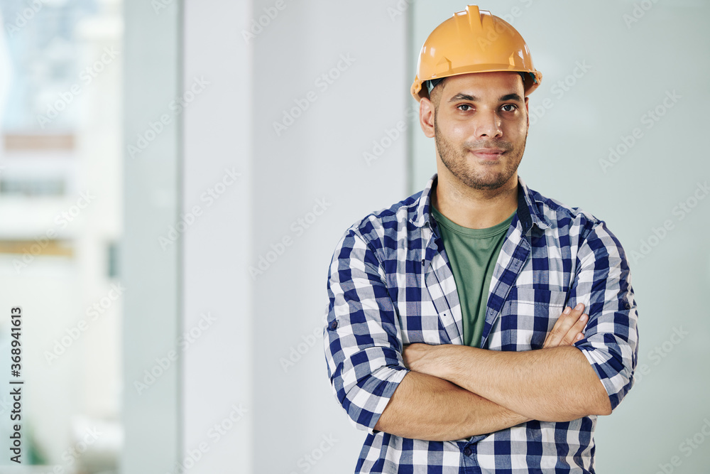Portrait of handsome smiling contractor in hardhat folding arms and looking at camera Portrait of handsome smiling contractor in hardhat folding arms and looking at camera